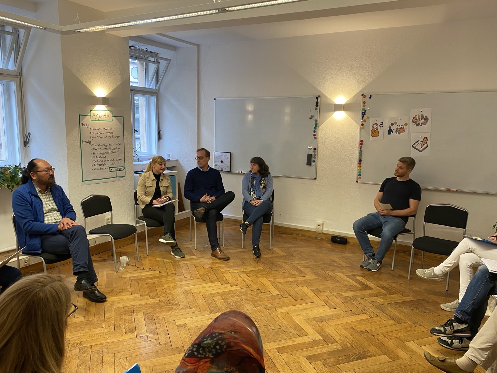 Personen sitzen auf Stühlen im Halbkreis.