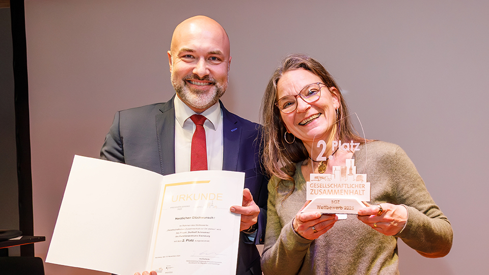 Ein Mann und eine Frau stehen nebeneinander und präsentieren eine Urkunde und eine Pokal.