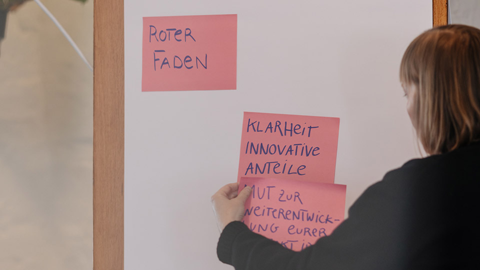 Eine Frau pinnt einen Zettel an eine Metatafel.