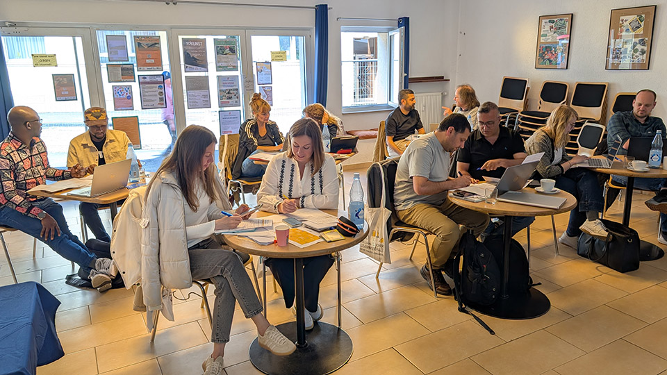 Mehrere Menschen sitzen in kleinen Gruppen an Tischen und unterhalten sich.