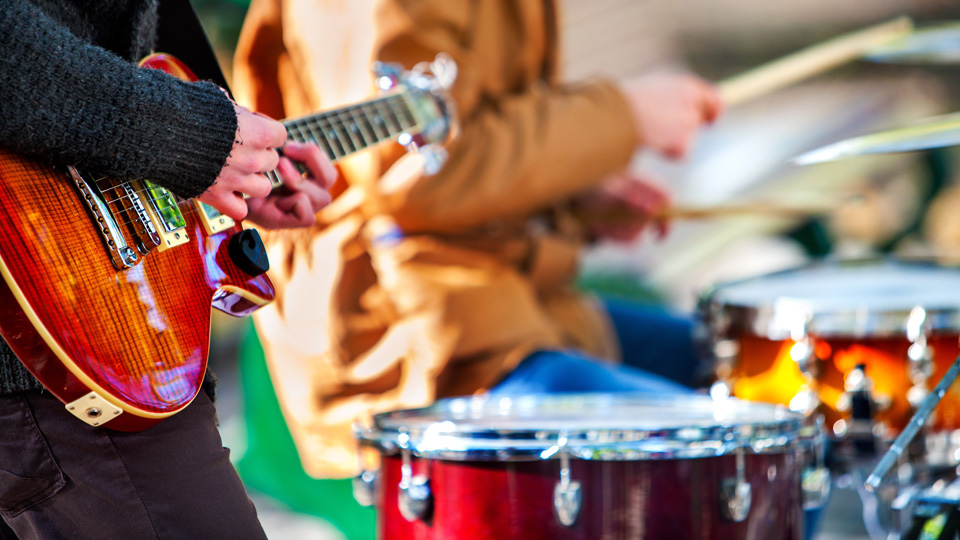 Nahaufnahme einer von Männerhänden gespielte Gitarre und eines Schlagzeuges