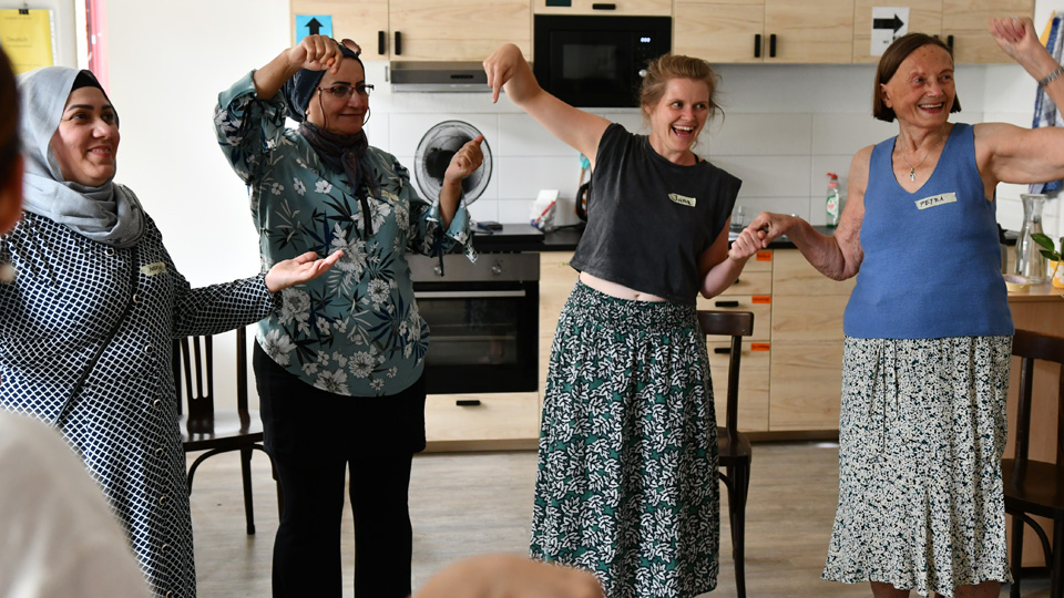 Vier Frauen stehen in einer Küche nebeneinander im Halbkreis, lachen und tanzen.