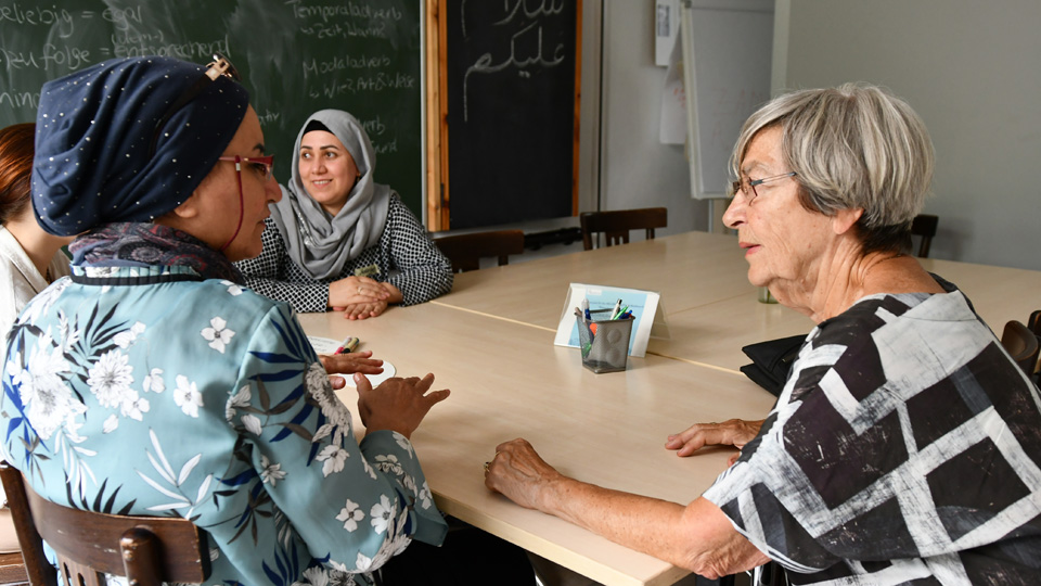 Vier Frauen sitzen in einem Klassenzimmer an einem Tisch und unterhalten sich.