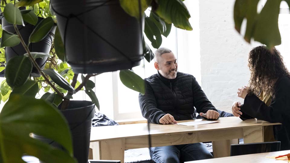 Ein Teilnehmer und die Leiterin einer Projektschmiede sitzen an einem Tisch und unterhalten sich.